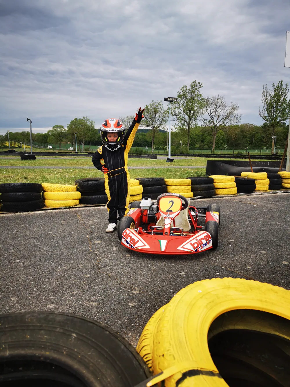 Un enfant pilote, bras levé, à côté de son kart