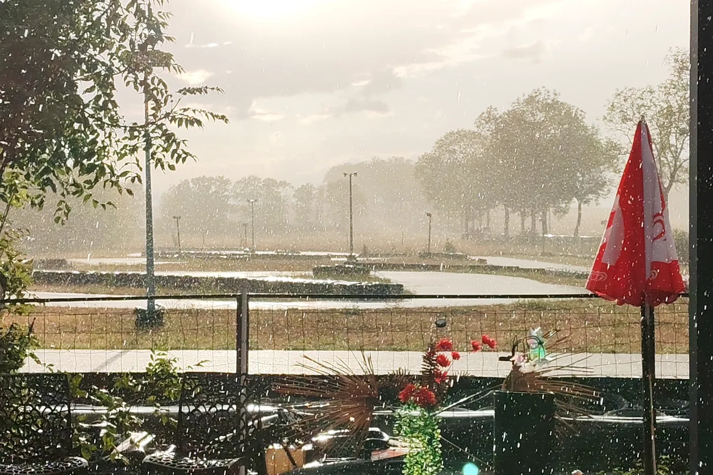 La piste sous l'averse vue depuis la terrasse, parasol rouge au premier plan
