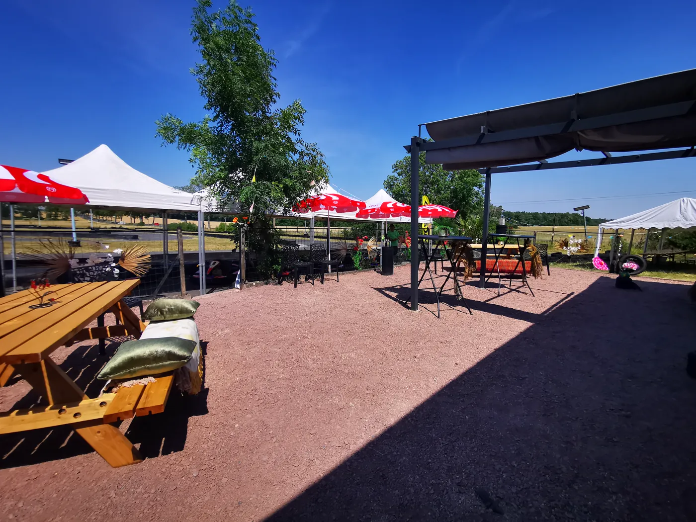 La terrasse de Kart'Hell au soleil, tables en bois et parasols rouges